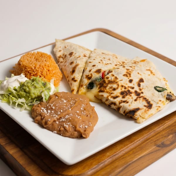 A quesadilla with melted cheese, rice, refried beans, guacamole, and sour cream on a white plate.