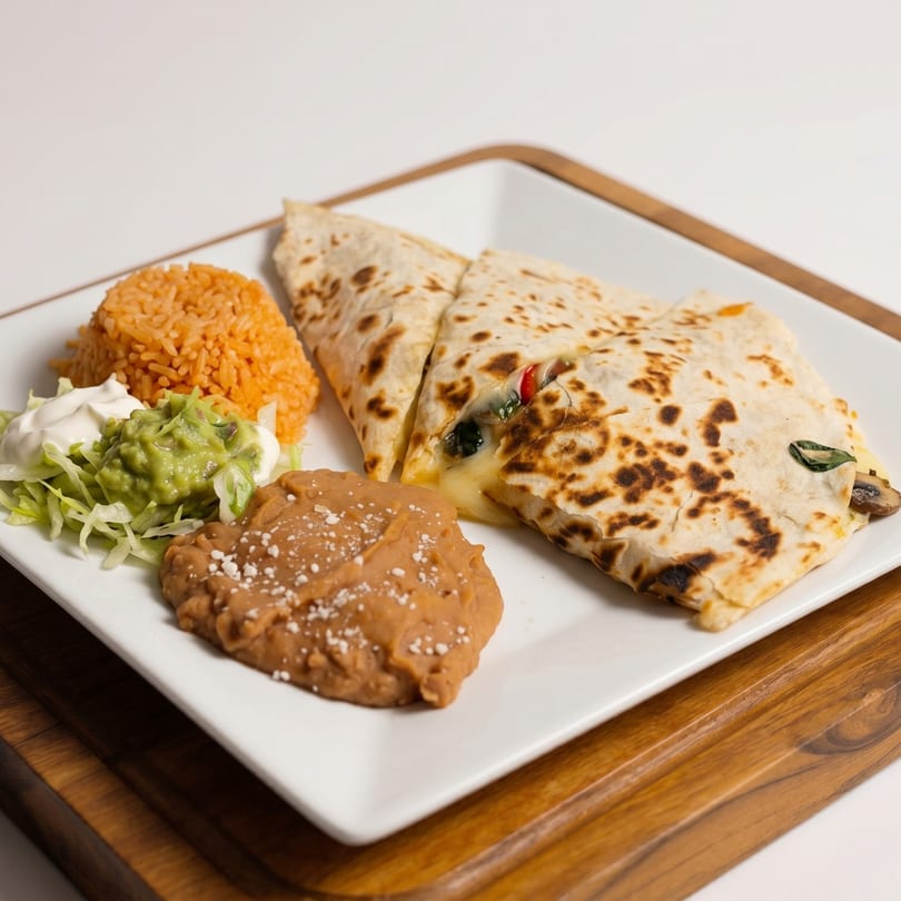 A quesadilla with melted cheese, rice, refried beans, guacamole, and sour cream on a white plate.